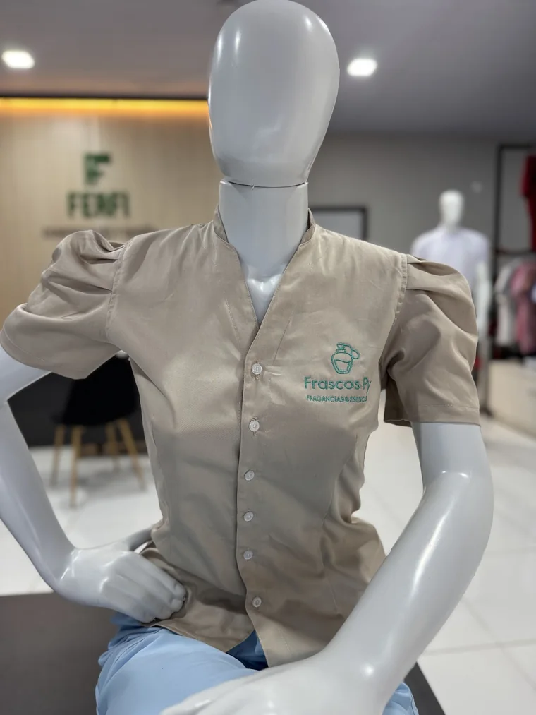 Blusa beige con logo bordado en un maniquí, con el showroom de FERFI y el logo de la marca en la pared